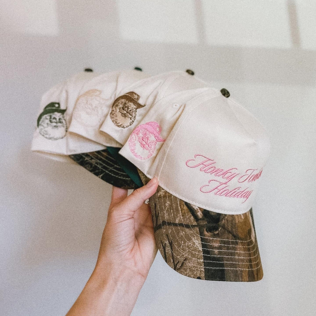 Hand holding a camouflage-patterned cap with floral designs and text against a white background
