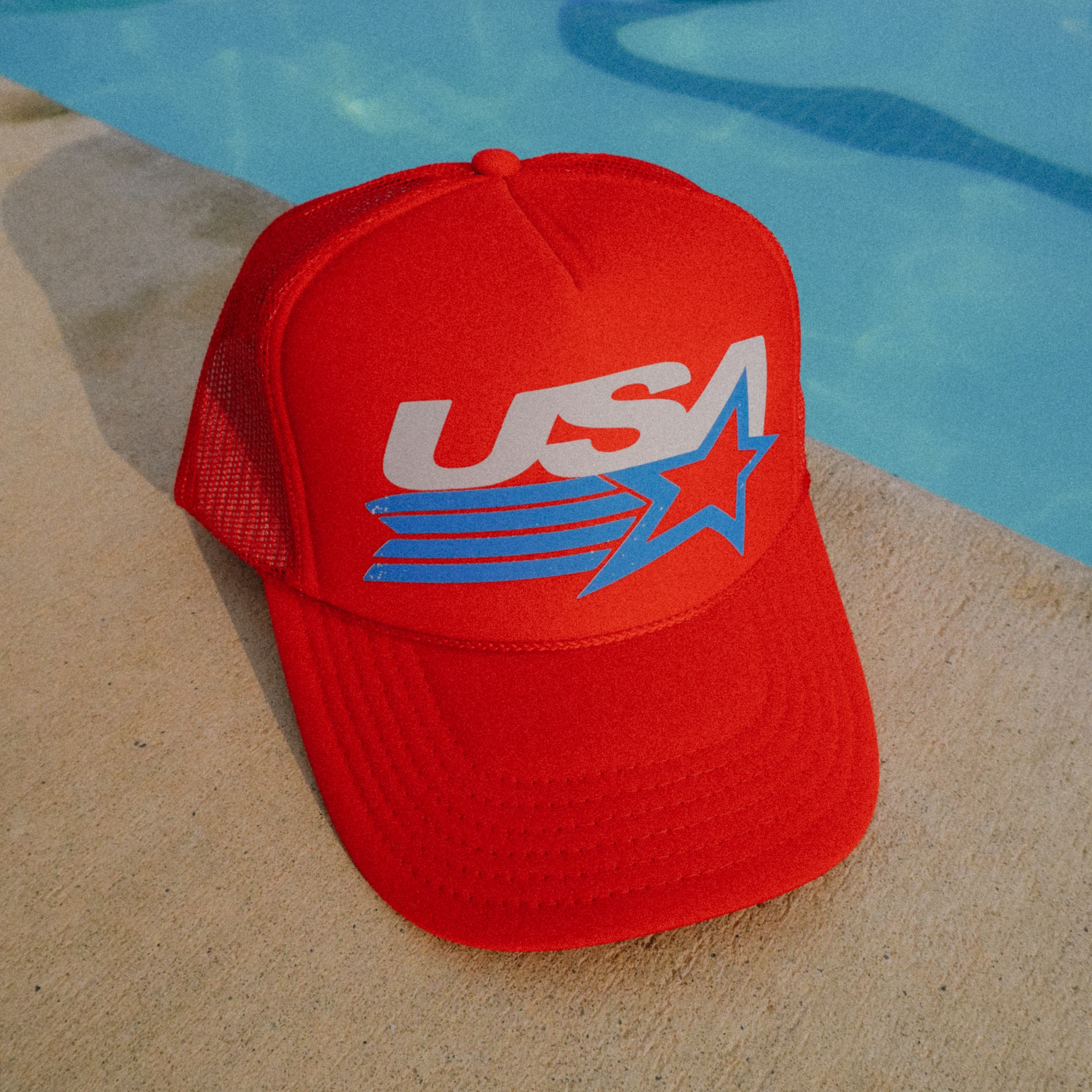 Red cap with 'USA' logo on a poolside surface