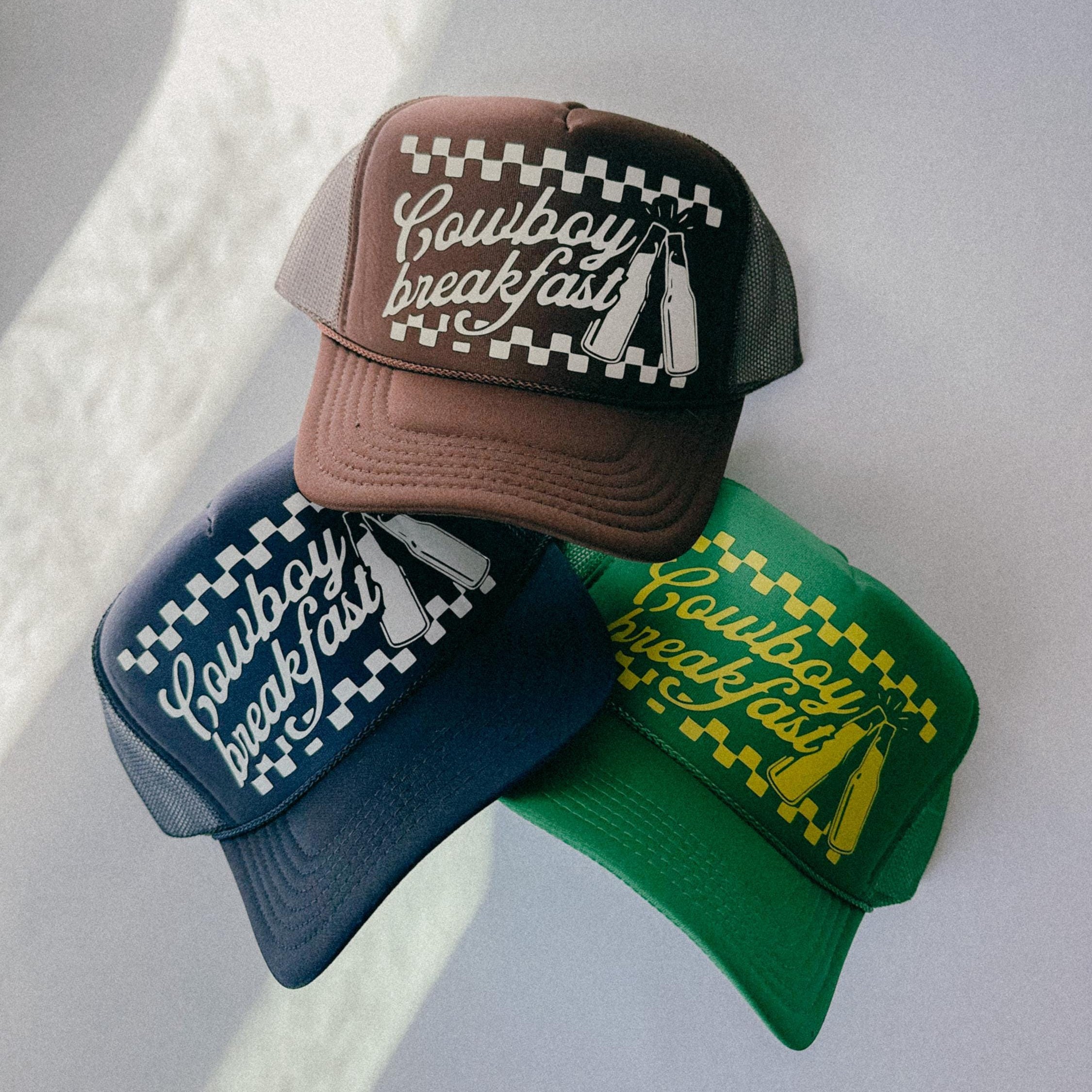 Three baseball caps with 'Cowboy Breakfast' text on a light gray background